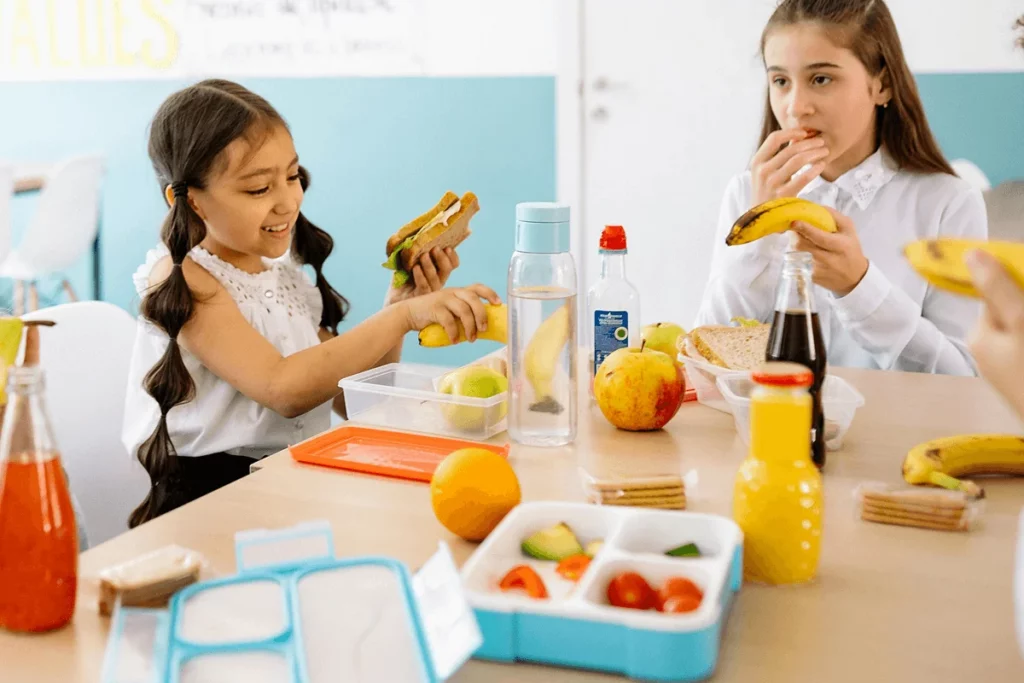 Zwei Kinder essen in der Pause aus ihren Brotdosen an der Schule am Mohnweg