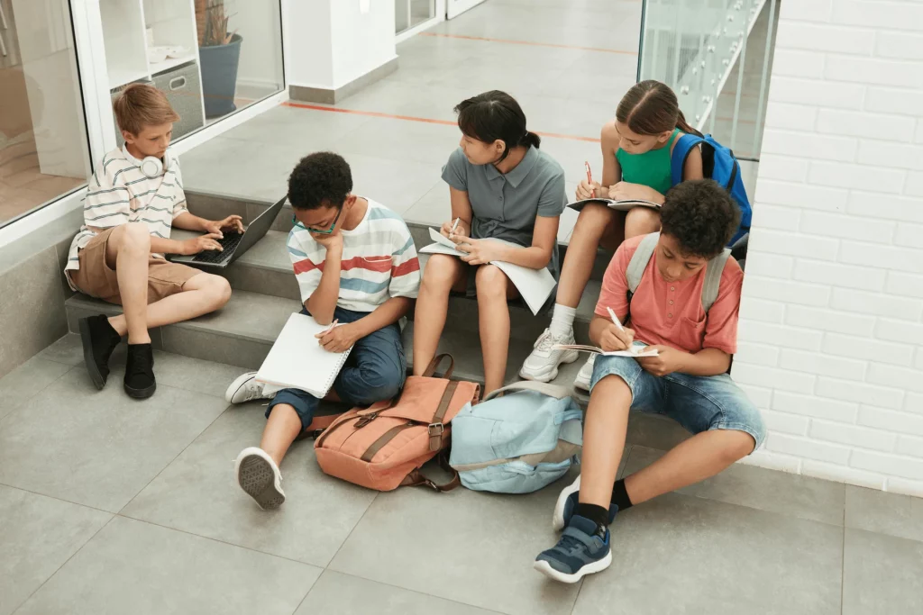 Kinder arbeiten auf dem Schulflur der Grundschule am Mohnweg mit Aufgaben und Laptop